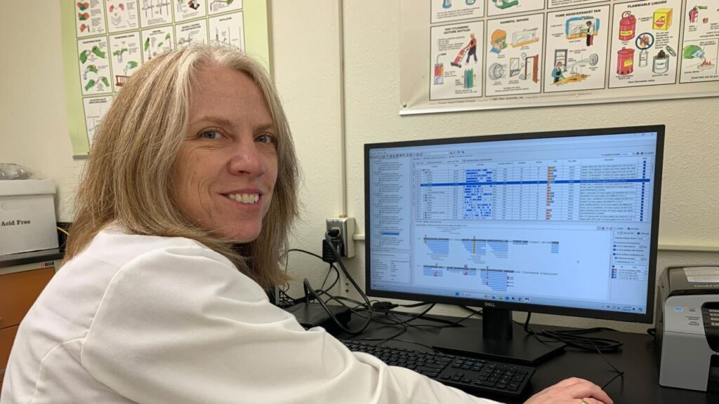 Woman dressed in lab coat looking at data on a computer screen